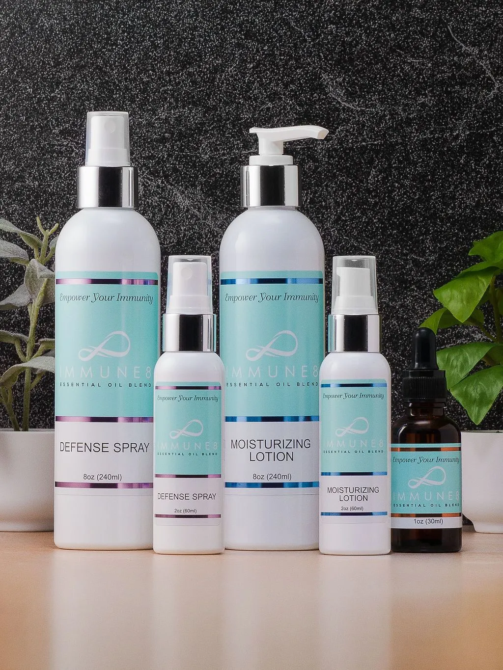 The image features a collection of five skincare products, including spray, lotion, and oils, displayed on a surface with a dark textured background and greenery.