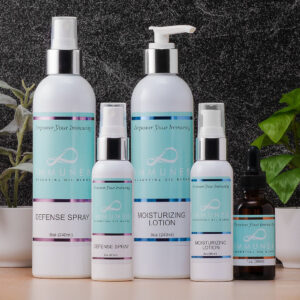 The image features a collection of five skincare products, including spray, lotion, and oils, displayed on a surface with a dark textured background and greenery.